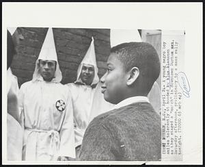 A young negro boy smiles tolerantly at hooded ku klux klansmen as they staged a "march" in downtown Durham. Saturday afternoon, preliminary to a mass rally tonight.