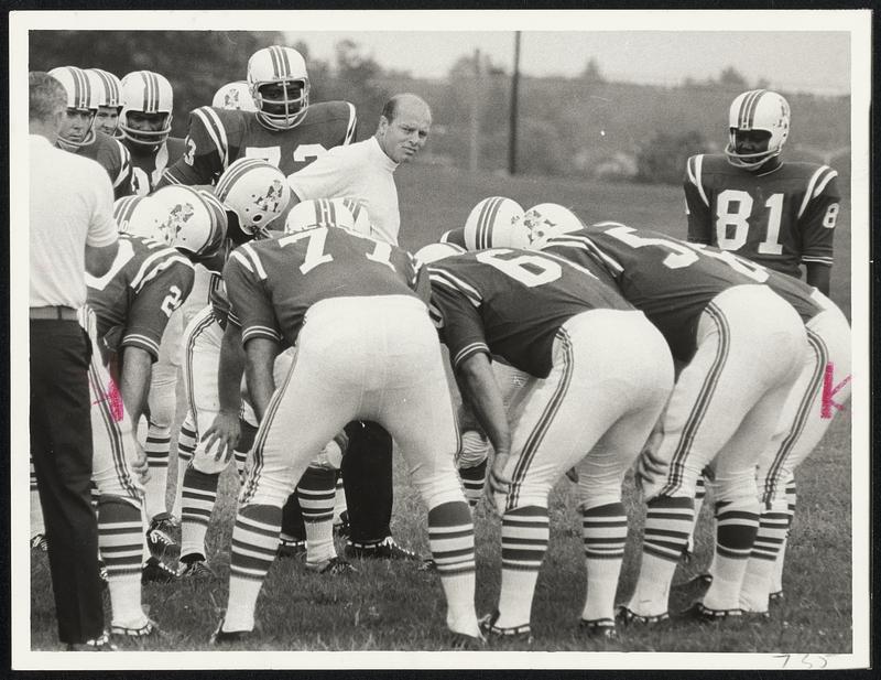 Checking His Charges - New Patriots coach Clive Rush, in center of huddle, inspects his troops yesterday in opening-day drills at University of Massachusetts training camp.