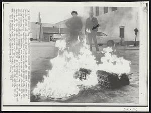Induction Records Set Ablaze--Flames consume records of 231 men scheduled for induction into the armed services at Los Angeles today. Watching the fire are Charles Friend, left, 22, and Walter Skinner, 25, of Pasadena, who were arrested and charged with suspicion of conspiracy to commit burglary. Police said they seized the records at the induction station, drove to a parking lot a block away, and used napalm to set the papers on fire, then waited for arrest. The 231 men were referred back to their draft boards for reprocessing.