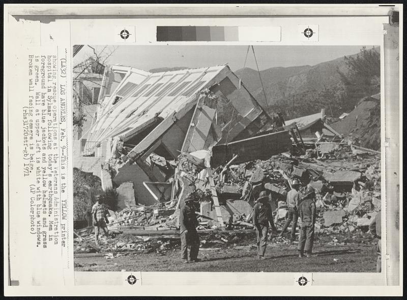 This is the Yellow printer showing rescue operations at the Veterans Administration hospital in Sylmar following today's earthquake. Men in foreground have blue jackets and yellow helmets and grass is green. Wall at upper left is white with blue windows. Broken wall facing camera is beige.