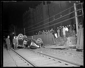 People gather by a car overturned on the railroad tracks