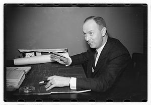 A man seated at a desk, blueprints in front of him