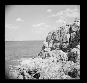 People on rock outcropping, sailboats in distance