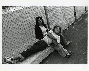 Two girls on stone bench next two a fence