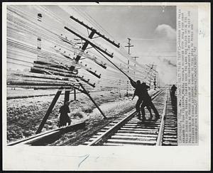 Ice Halts Train Traffic--Workmen with poles attempt to push telegraph poles, heavily weighted with ice, from over train tracks here today. Traffic over the line was halted until the poles could be pushed clear of the right-of-way. Two days of sleep and freezing rain caused extensive damage in this area to power and communication lines.