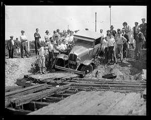 People posing around a car which has stopped off the road, possibly in an accident