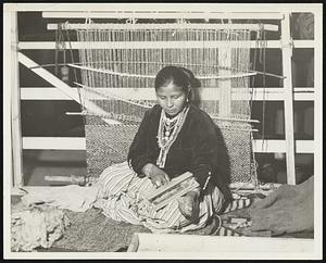 This Indian woman is one of the skilled Navajo rug makers now demonstrating this fascinating art at the R.H. White company store. Because of the popularity of these rugs, this demonstration is educational and instructive.