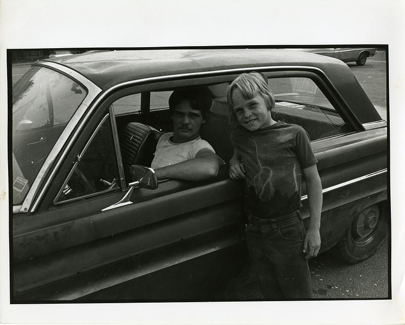 Man sitting in car while a child leans against the car