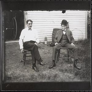 Two men sitting in front of barn