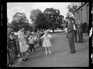 Jackie & JFK watch [girl] with hula hoop on visit to a school yard