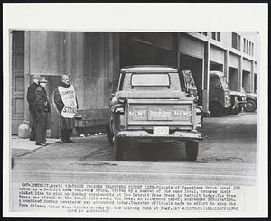 Truck Crosses Teamsters Picket Line - Pickets of Teamsters Union Local 372 watch as a Detroit News delivery truck, driven by a member of the same local, crosses their picket line to pick up Sunday supplements at The Detroit Free Press in Detroit today. The Free Press was struck by the local this week, The News, an afternoon paper, suspended publication. A combined Sunday newspaper was announced today. Teamster officials made no effort to stop the News drivers. Other News trucks appear at the loading dock at rear.