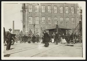 This picture presents a typical scene in Passaic, N.J., in which city thousands of workers in the textile mills have struck for higher wages. Workers are shown leaving the mills as soon as the strike was declared.