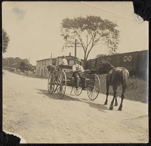 Two men in a horse-drawn wagon near railroad