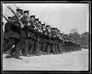 A line of men in military uniform marching, all holding rifles