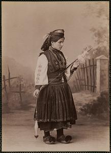 Studio portrait of woman in traditional Greek dress using drop spindle