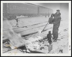 Blowing Hot And Cold is Charles Peterson of Reading, working to thaw out a frozen switch in the Boston & Maine Railroad yards as second blizzard in three days overspreads Boston, snarling transportation. Commuter trains generally fought an unequal battle against the storm.