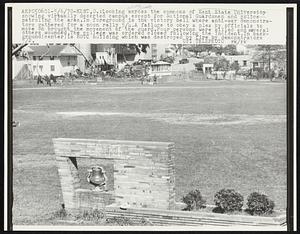 Looking across the commons of Kent State University showing virtually deserted campus except for National Guardsmen and police patrolling the area. In foreground is the victory bell where anti-war demonstrators gathered for a noon rally 5/4. A failure to obey a plea by officials to move on brought the movement of the guard. Four persons were killed and several others wounded. The college was ordered closed following the incident. In background (center) is ROTC building which was destroyed by fire by demonstrators 5/2.
