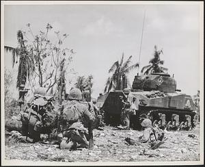 Marine Corps tank stands by as two leathernecks sharp shooters take cover behind trees while attempting to pick off the occupants of a Japanese pillbox on Guam
