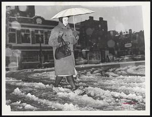 A woman walks through snow holding an umbrella