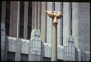 Closeup of a building façade, sculpture of a golden bird on a column in front