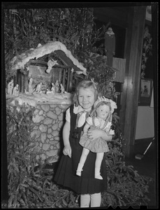Girl with doll in front of nativity scene