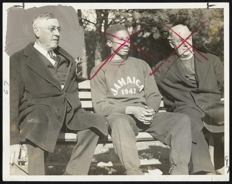 West Indies, Not Jamaica Plain, in Boston is signified by those letters on this Boston College freshman's sweat suit. He's Herbert McKenley, sprint champion from the island of Jamaica, one of two Jamaica boys awarded scholarships to Boston College by the Jesuit Fathers. On the left is Coach Jack Ryder and on the right is the Very Rev. Thomas J. Feeney, S.J., superior of the Jesuit mission in Jamaica. McKenley is taking a pre-medical course and plans to attend Georgetown dental school after completing his four years at B.C. He is 6 feet 2 inches tall and Coach Ryder plans to try him at the indoor 600-yard distance.