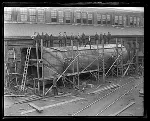 Workers posing with a large metal part, possibly of a ship