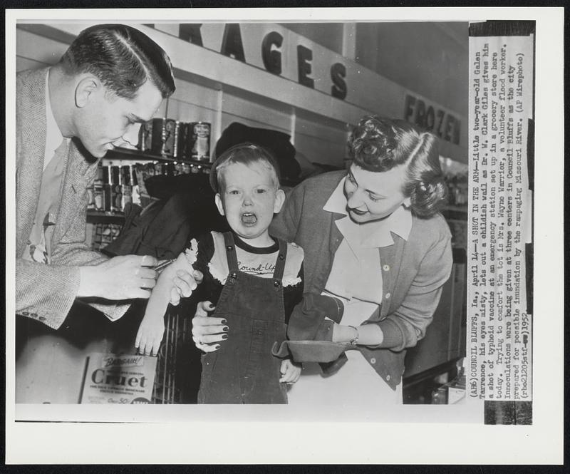 A Shot in the Arm -- Little two-year-old Galen Tarrence, his eyes misty, lets out a childish wail as Dr. W. Clark Giles gives him a shot of typhoid vaccine at an emergency station set up in a grocery store here today. Trying to comfort the tot is Mrs. Wayne Warrior, a volunteer flood worker. Innoculations were being given at three centers in Council Bluffs as the city prepared for possible inundation by the rampaging Missouri River.