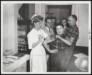 Stiffening Lip-A young patient at the Boston Evening Clinic, 314 Commonwealth avenue, anticipates the jab of a hypodermic needle wielded by Mrs. Ruth Taylor, supervisor of nurses, in an allergy clinic.