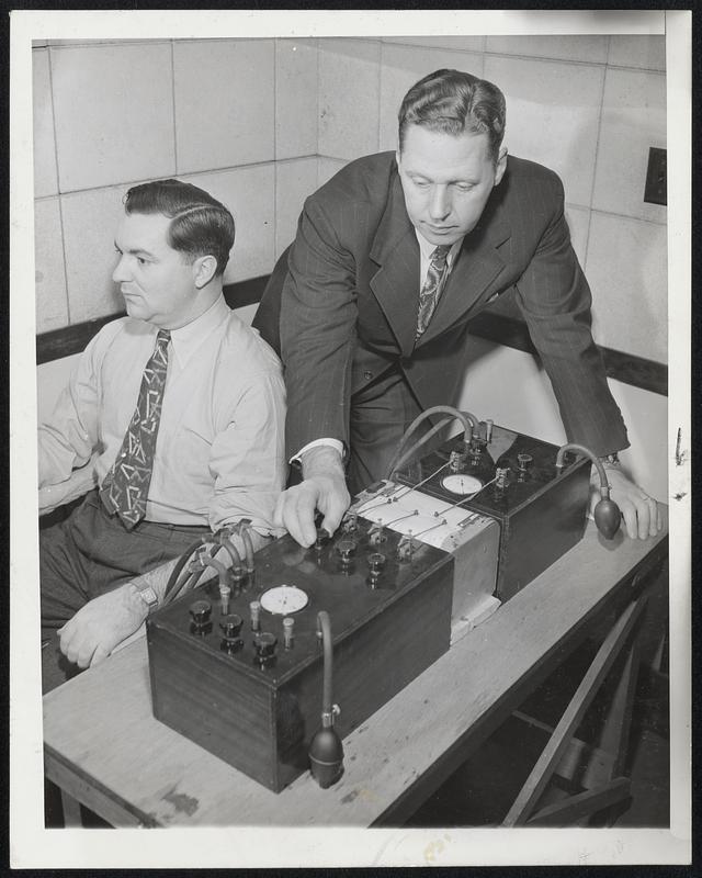 Improves Lie Detector--Richard E. Gorman (left). assists John E. Reid during a demonstration of Reid's lie detection equipment at the Chicago police department's scientific crime detection laboratory.