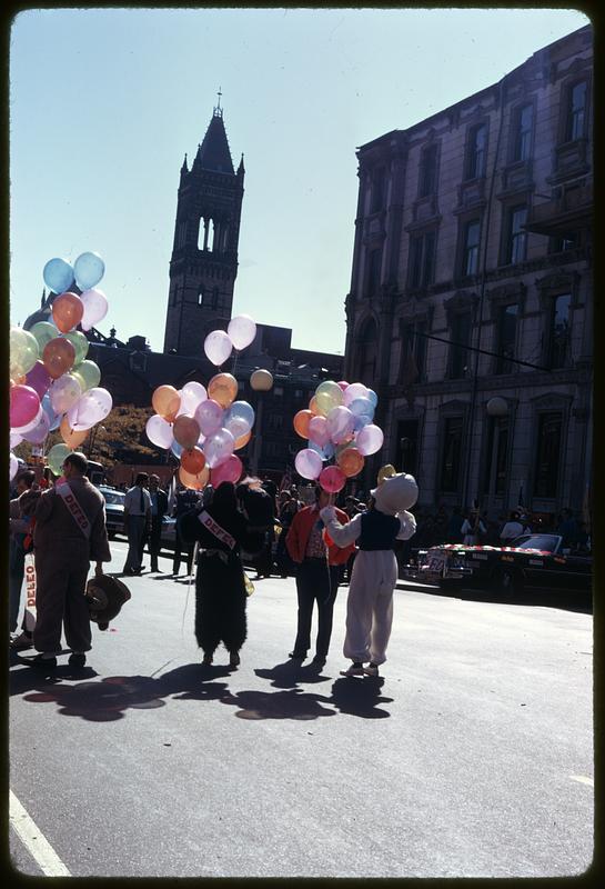 People holding balloons, some wearing mascot costumes, Old South Church in background, Boston Columbus Day Parade 1973