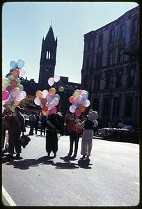 People holding balloons, some wearing mascot costumes, Old South Church in background, Boston Columbus Day Parade 1973