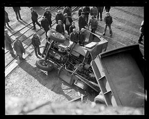 People gather by an overturned truck