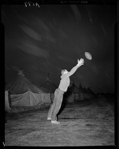 Man catching football outside military tents