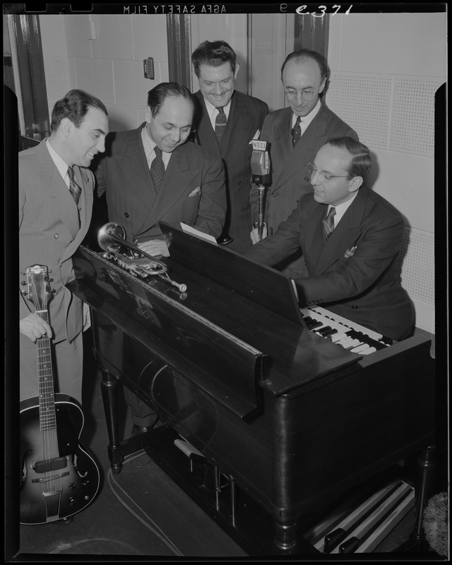 Five unidentified men, possibly including Frank Bolitzeo, around a piano, with microphone, trumpet, and guitar