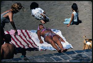 Children and sunbathing woman on beach, likely California