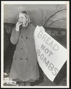 Fort Devens. Kathy Molan, stands with pickets for Anti-Johnson policy, she is eating bread, and bears, sign, “Bread Not Bombs”.