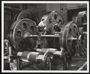 The wheels for Paul Bunyan's mighty watch might dwarf an ordinary man by comparison as much as these gears at the General Electric Company's Medium Team Turbine, Generator, and Gear Department here reduce the relative stature of the engineer shown. From front to rear: the two gears in the backgrounds are low speed pinions for a ship's propulsion gear set. The two in the middle are intermediate speed gears. And the others are low speed ship's propulsion gears.