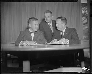 Three men looking at a binder