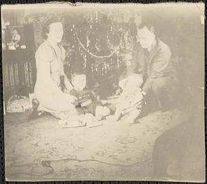 Man and woman with two toddlers sit in front of Christmas tree
