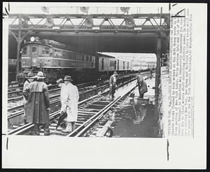 Rail Service Delayed--Officials and trackmen observe tracks flooded by rain water at the Mott Haven yards in the Bronx section of New York today. Train service into and out of Grand Central Terminal in Manhattan was temporarily interrupted for about an hour due to flood waters short circuiting electric power. In background is a stalled New York, New Haven and Hartford Railroad train which uses the yards with the New York Central Railroad.