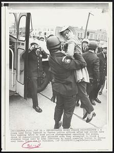 Newton, Mass. – Demonstrator Ducks Police Photographer – A young lady being carried by Newton police officer after her arrest here this morning tries to duck police photographer recording the scene. About 40 demonstrators were arrested when they attempted to block a stairway being used by Army inductees to board commuter trains to Boston Army Base. There was no violence.