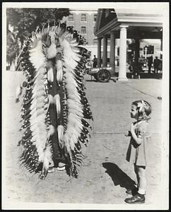 Indian in War Bonnet-This is not a strutting Thankgiving turkey with outspread tail feathers but a Sioux Indian brave at Mandan, S. D., who proudly displays his remarkable feathered warbonnet for the benefit of the little miss from the East.