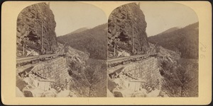 Railroad tracks on a mountainside, supported by a stone wall