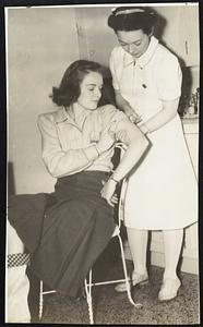 Fighting the Flu--Miss Margaret Butler (seated), student at the University of Kansas, receives a "shot" of the new influenza vaccine developed by the Rockefeller Institute. Administering the vaccine is Nurse Louise Rundell.