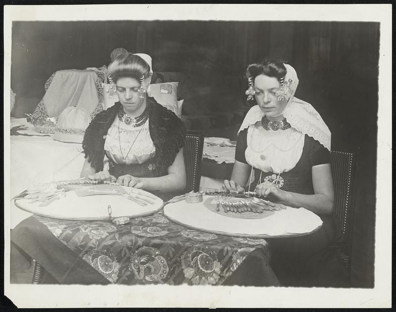 Holland to Revive Lace-Making. In an effort to revive the old art of lace work, the Dutch Government has approved the holding of large exhibitions of various modes of lace in the various cities and towns of Holland. Photo shows two girls of Zeeland in their national costume, at work on some lace pattern.