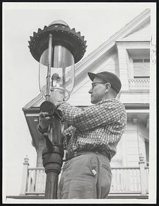 Modern Lamplighter -- He's James Flynn shown atop the crossbar of tis lamp on Wellesley place in Dorchester, one of 270 gas lamps left.