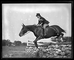 Horse and rider jumping over a low stone wall