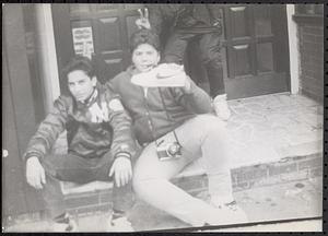 Three young men on the steps in front of Nick's Steak House, one holding a sneaker