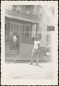 A man stands in front of a house wearing sunglasses